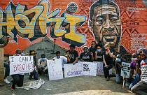 Protesters against police violence gather next to a new mural painted this week showing George Floyd with the Swahili word 
